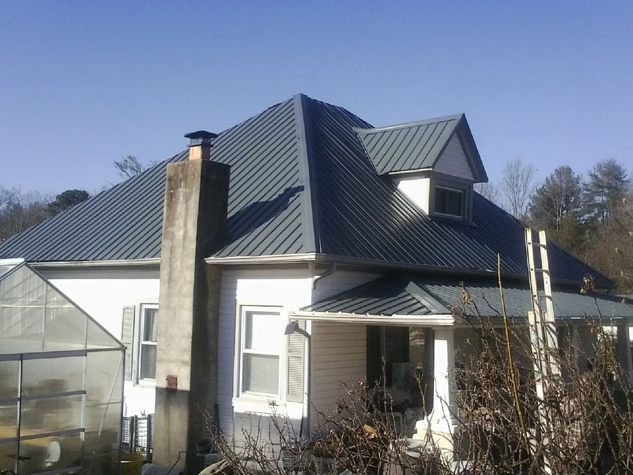 Dark blue standing seam metal roof on a white farmhouse with dormer — Slate & Tile Roof Repair by Roofing Brothers in Rowland Heights