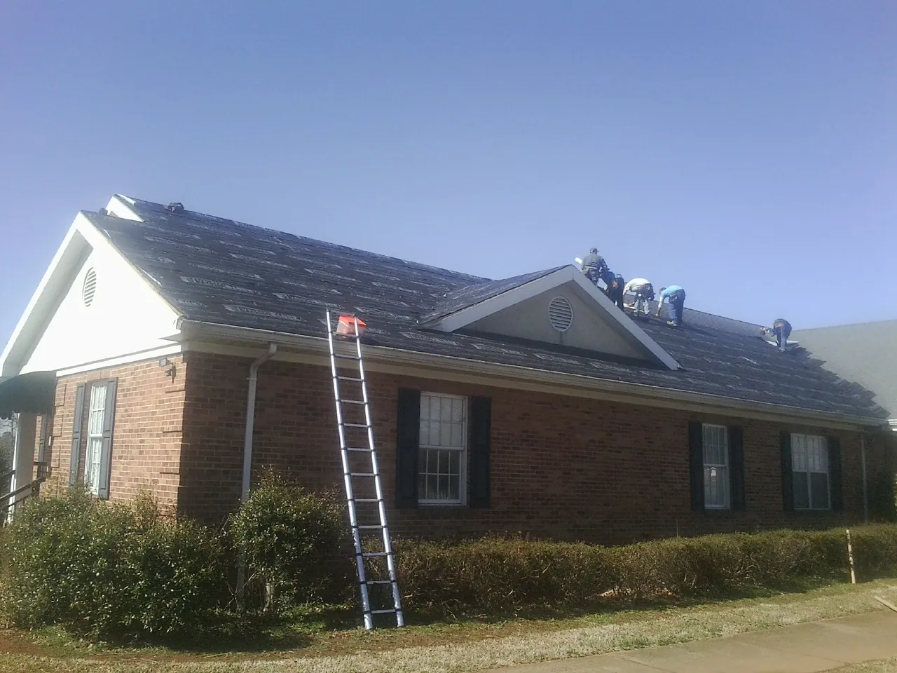 Crew tearing shingles off a brick ranch roof with a ladder set — Metal Roof Repair work by our crew in Rowland Heights