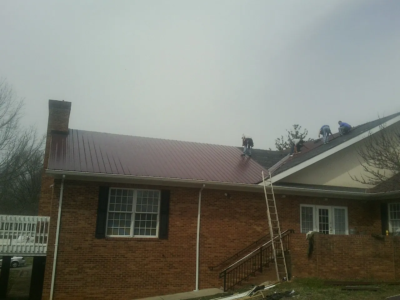 Crew setting red metal roofing panels on a brick home in Rowland Heights