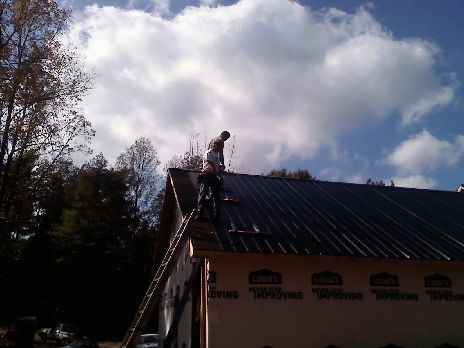 Roofer fastening dark metal panels high against a cloudy sky, from a Roof Inspection job in Rowland Heights