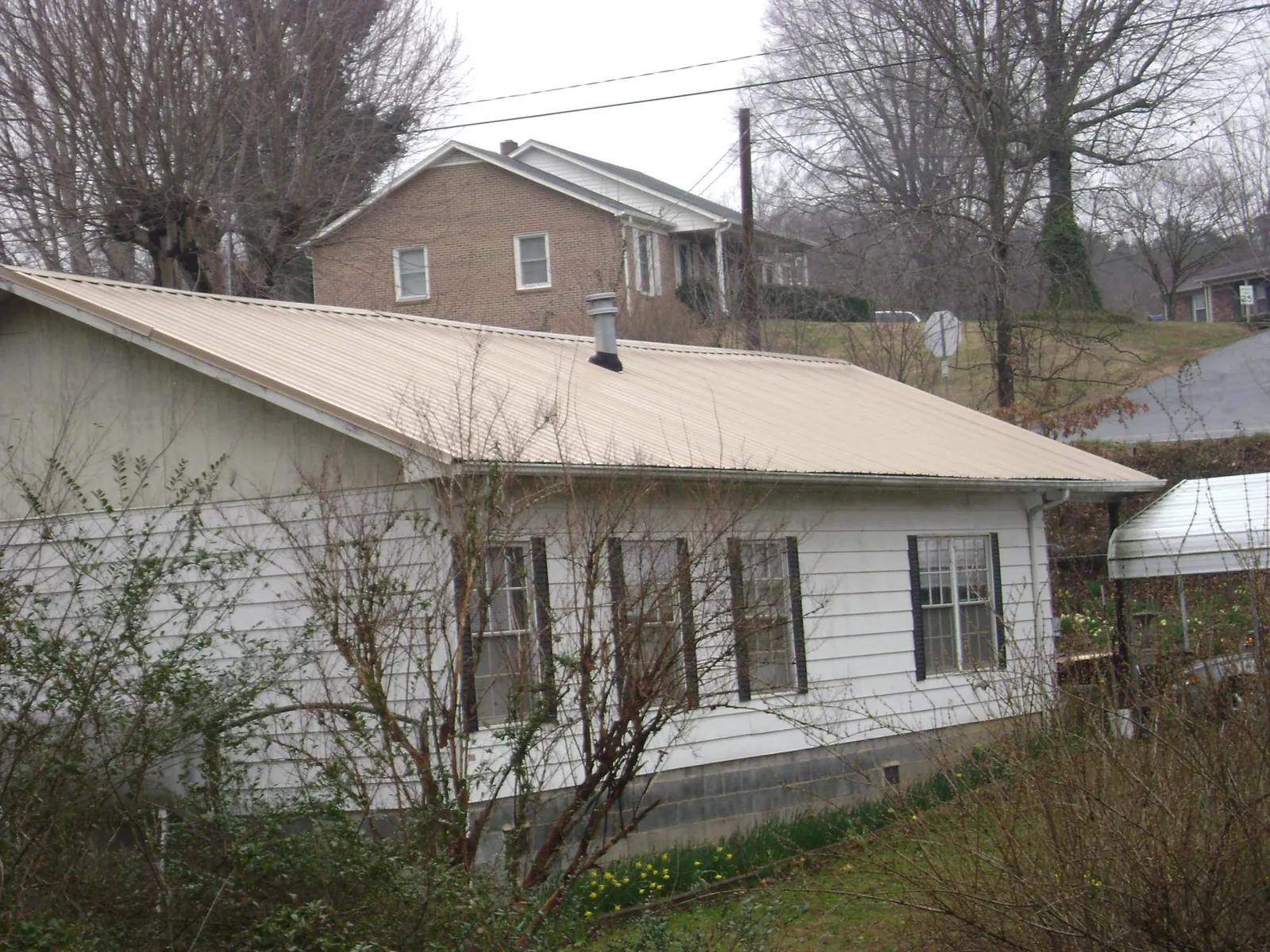 Tan metal roof on a white sided house set into a hillside — Commercial Roofing by Roofing Brothers in Rowland Heights